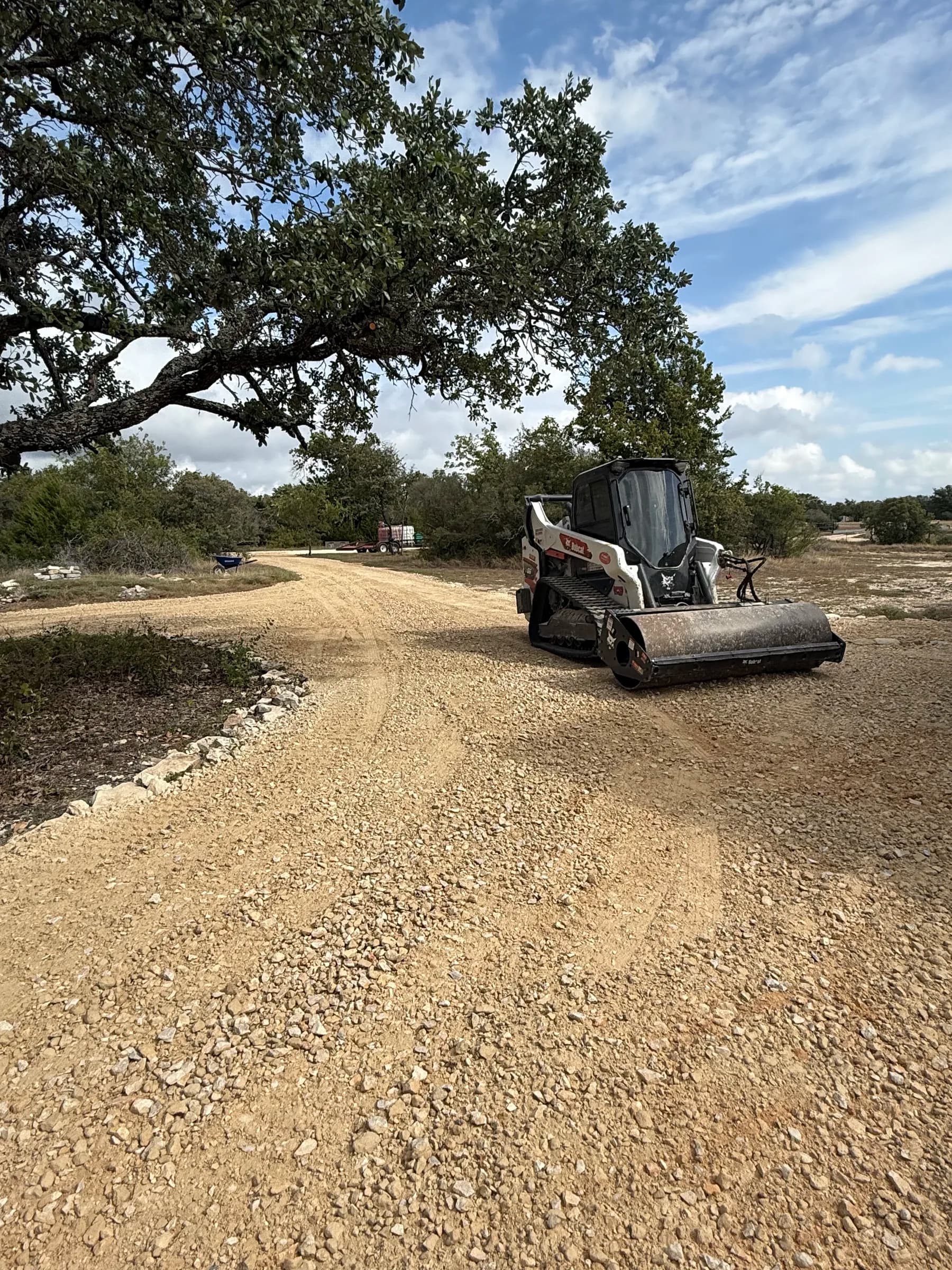 Skid steer grading the aggregate driveway beneath the trees in Ding Dong